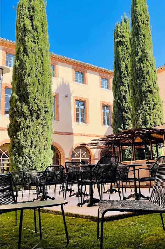 Terrasse extérieure du Bistro Salvador Dali dans la cour de l’Abbaye des Capucins à Montauban, avec tables, chaises et cyprès